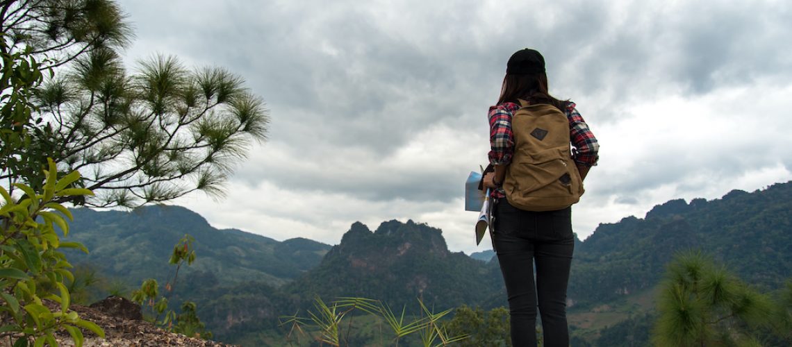 Women traveler with backpack checks map to find directions in wilderness area